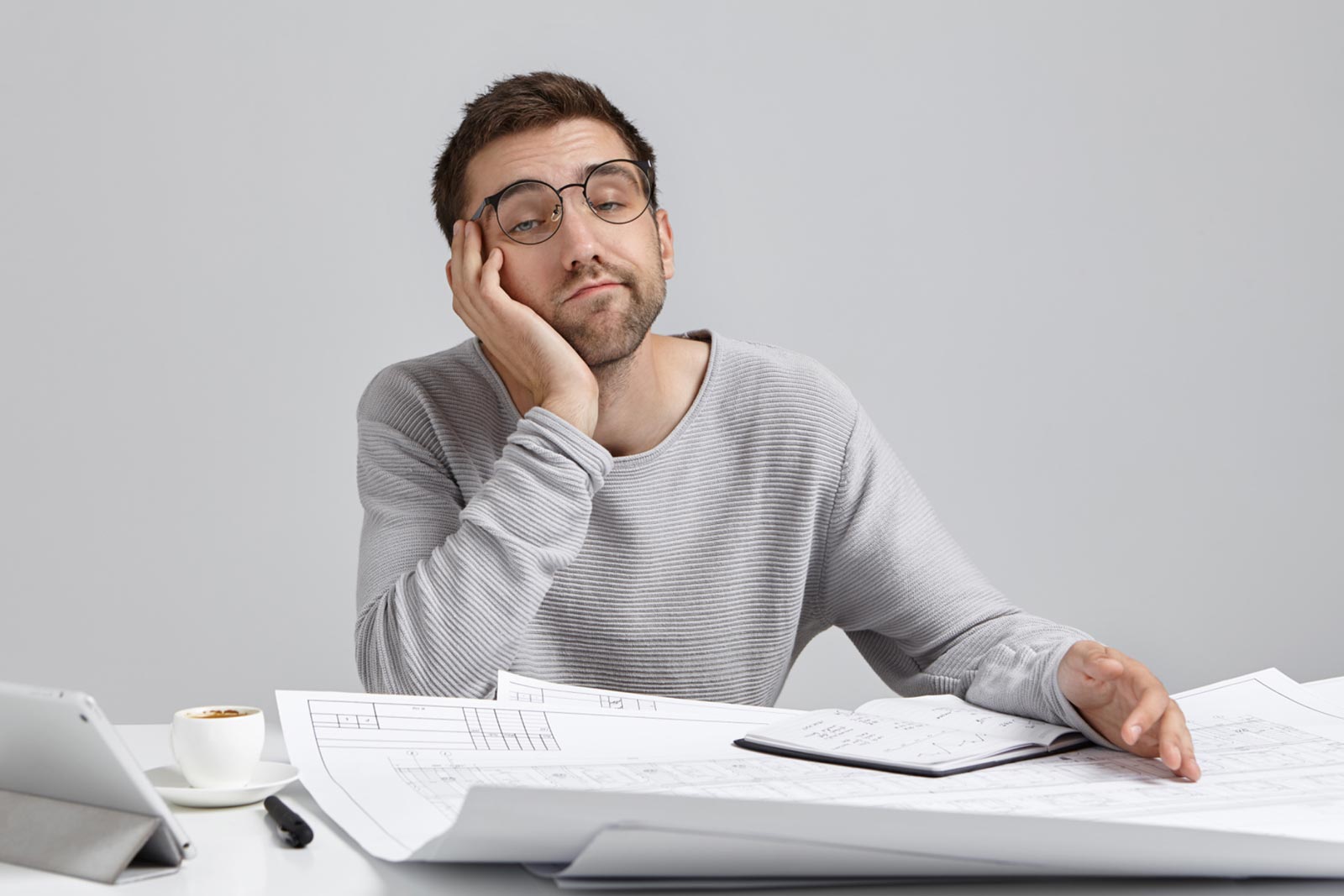 Mann mit Brille sitzt ratlos vor Plänen und Notizbuch am Schreibtisch