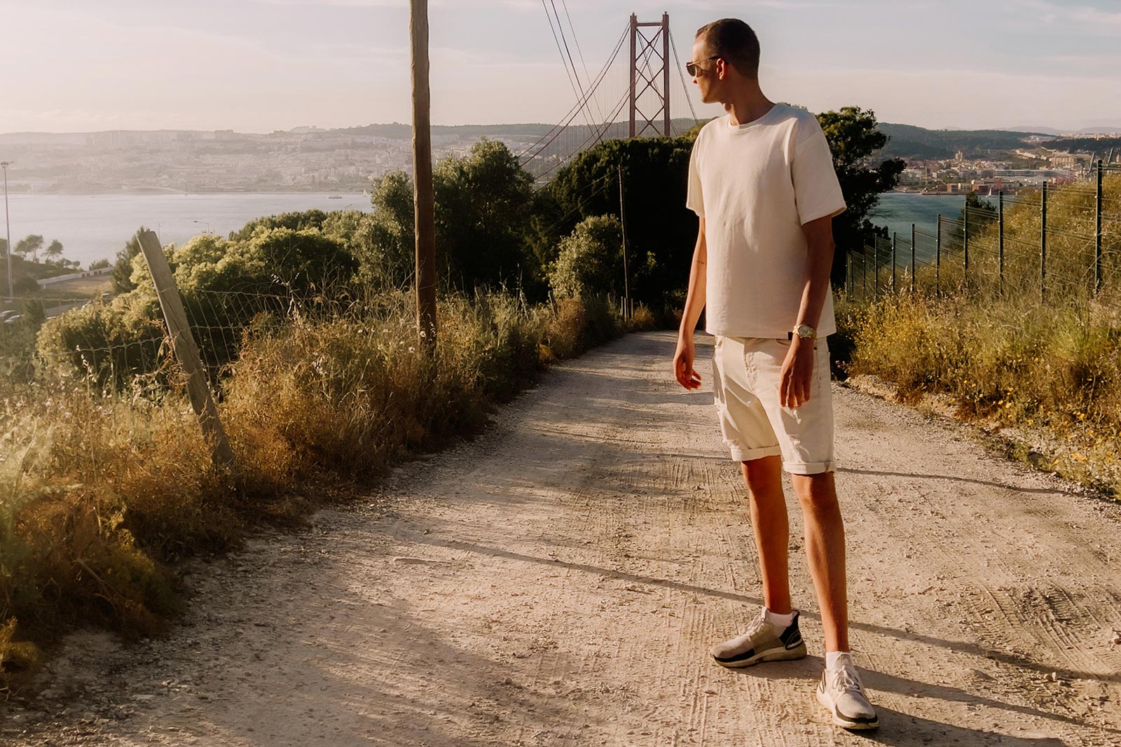 Lukas Zischke auf einem Sandweg über Lissabon, dahinter die Ponte 25 de Abril