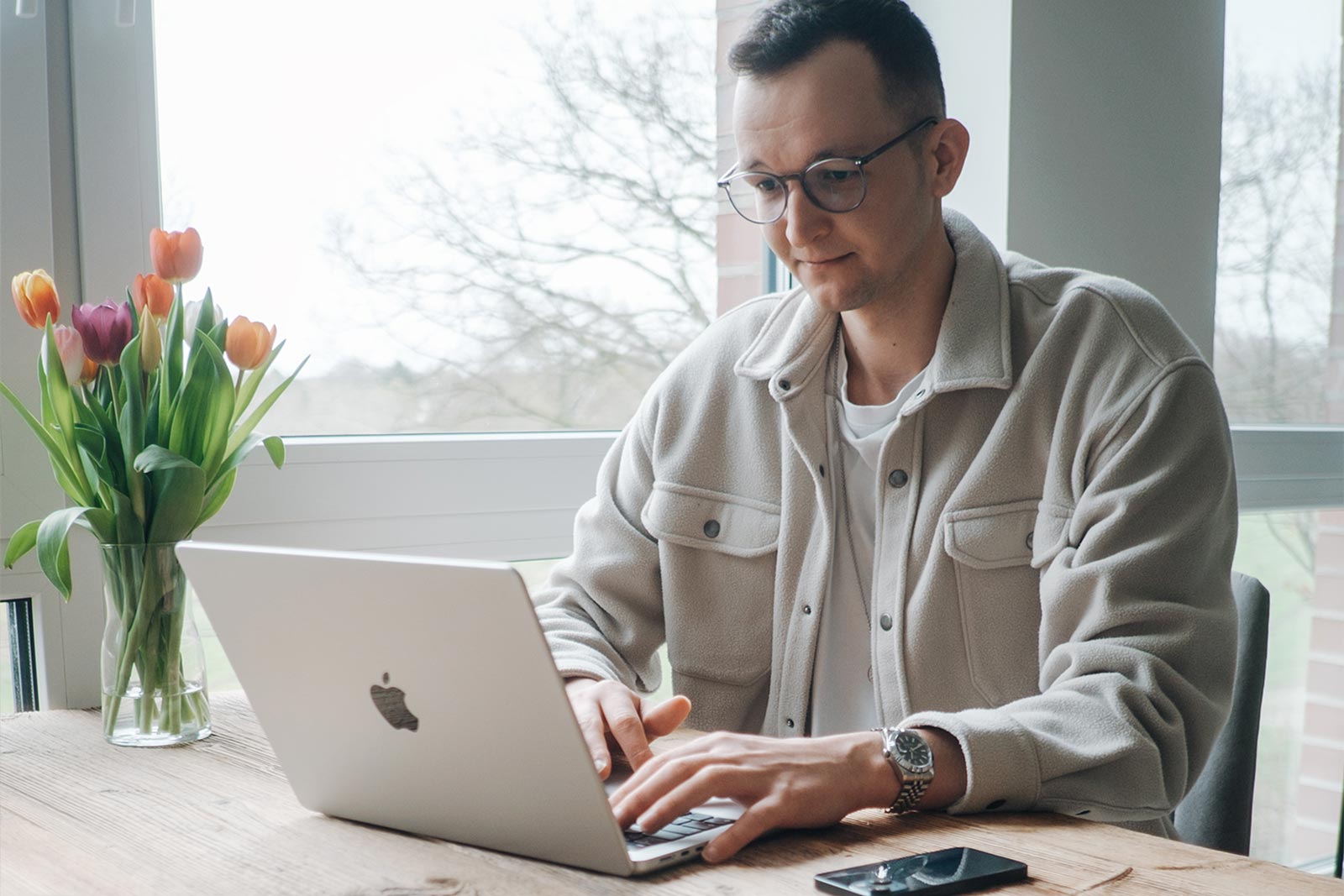 Lukas Zischke am Laptop an einem Fenster, daneben ein Strauß Tulpen